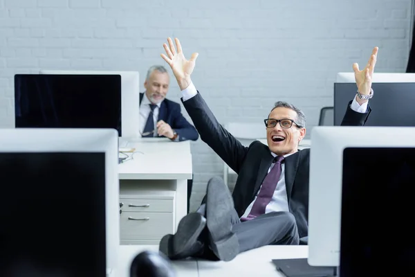 Selective focus of happy businessman sitting at workplace with legs on table — Stock Photo