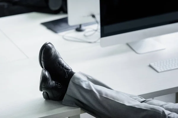 Tiro cortado de homem de negócios sentado no local de trabalho com as pernas na mesa — Fotografia de Stock