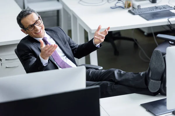 Cheerful businessman in eyeglasses sitting at workplace in office — Stock Photo