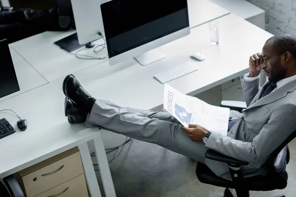 African american businessman reading newspaper at workplace — Stock Photo