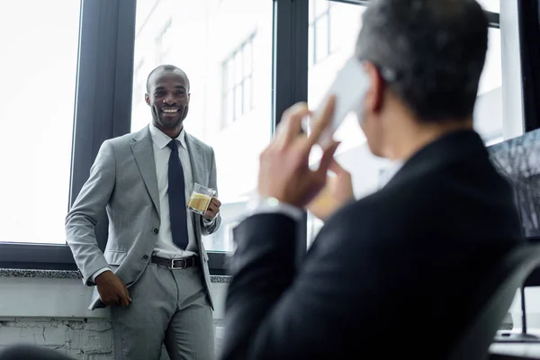 Selective focus of african american businessan looking at colleague talking on smartphone in office — Stock Photo