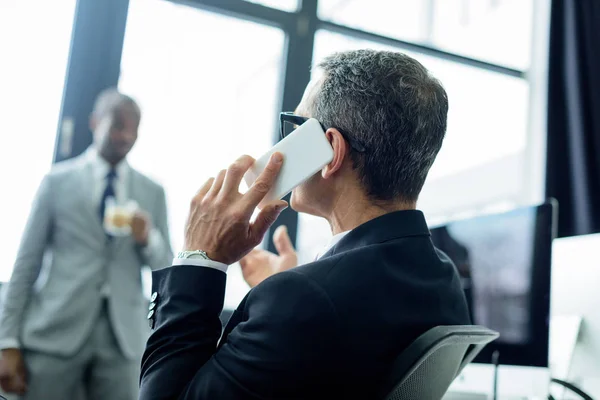 Selektiver Fokus des Geschäftsmannes, der im Büro mit dem Smartphone spricht — Stockfoto