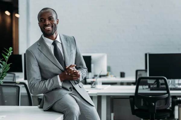 Sonriente hombre de negocios afroamericano sentado en la mesa en la oficina - foto de stock