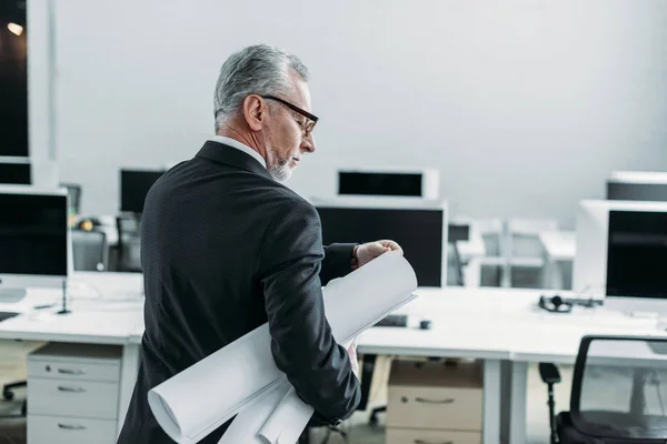 Back view of senior businessman with blueprints in office — Stock Photo