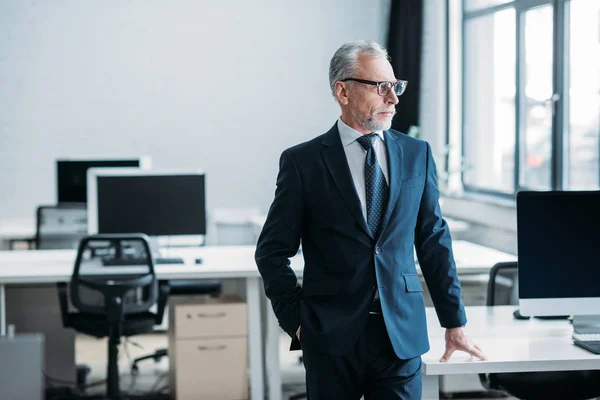 Senior businessman in eyeglasses standing at workplace in office — Stock Photo