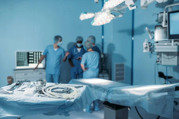 Four multiethnic surgeons in operating room with tools on foreground — Stock Photo