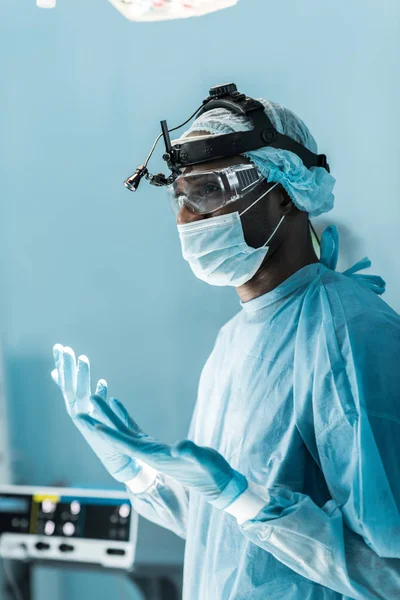 Vue latérale du chirurgien afro-américain en gants médicaux dans la salle d'opération — Photo de stock