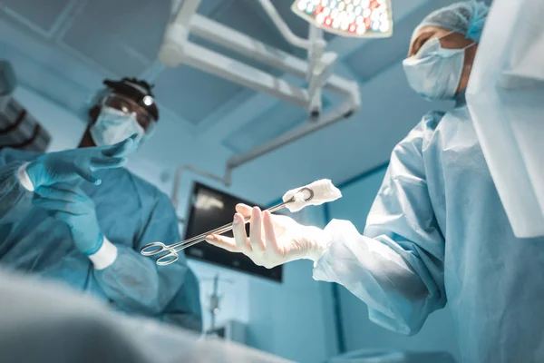 Bottom view of doctor passing medical clamp to african american surgeon — Stock Photo