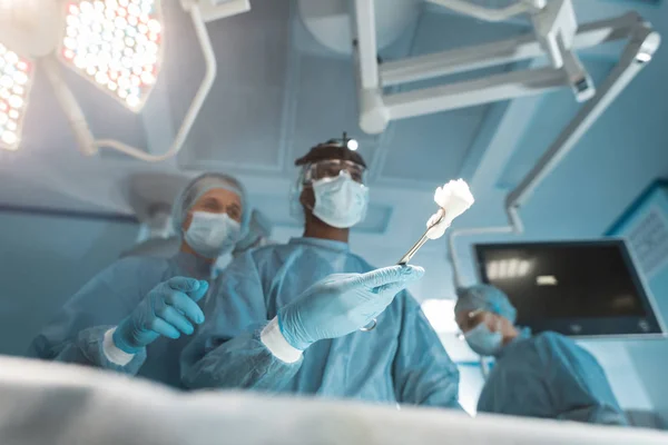 Vue du bas des chirurgiens multiculturels avec des outils pendant la chirurgie — Photo de stock