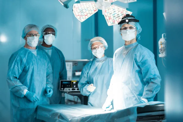 Cuatro doctores multiculturales mirando la cámara en el quirófano - foto de stock