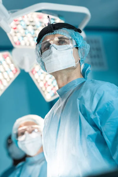 Vista inferior del cirujano en máscara médica mirando hacia otro lado - foto de stock