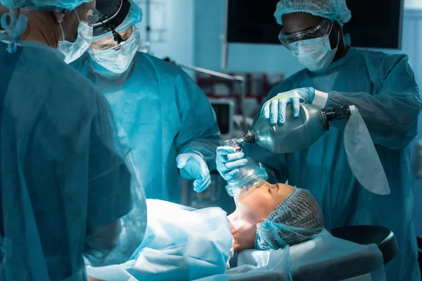 Anestesista afro-americano segurando máscara de oxigênio acima do paciente na sala de cirurgia — Fotografia de Stock