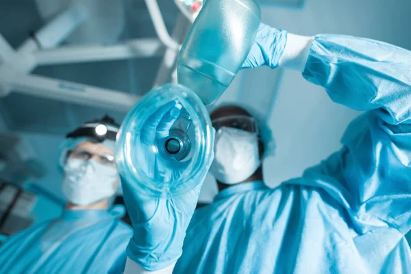 Bottom view of african american anesthetist holding oxygen mask above patient — Stock Photo