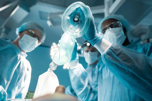 Vista dal basso dell'anestesista afro-americano con maschera di ossigeno sopra il paziente in sala operatoria — Foto stock