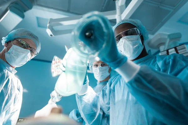 Vue du bas de l'anesthésiste afro-américain tenant un masque à oxygène au-dessus du patient — Photo de stock