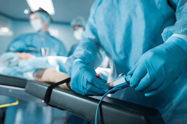 Image recadrée du médecin portant un oxymètre de pouls sur le doigt du patient dans la salle d'opération — Photo de stock