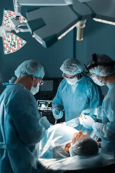 Cirujanos multiétnicos operando al paciente en quirófano - foto de stock
