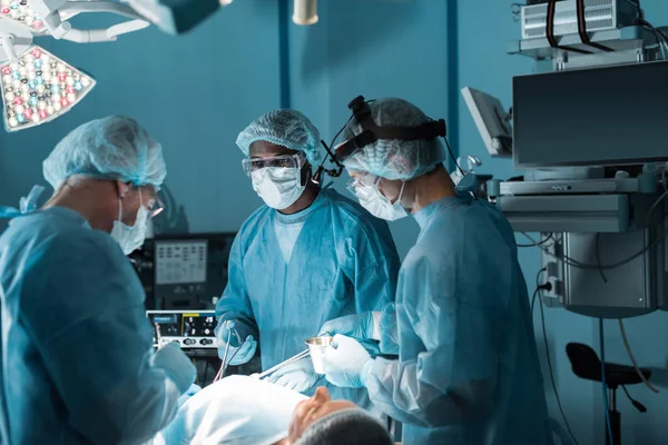 Cirujanos multiculturales operando al paciente en quirófano - foto de stock