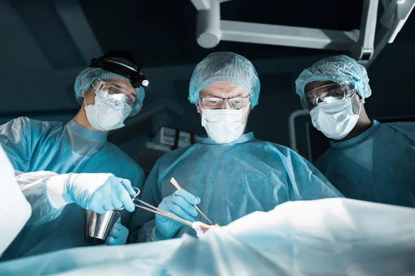 Cirujanos multiculturales operando al paciente en quirófano - foto de stock