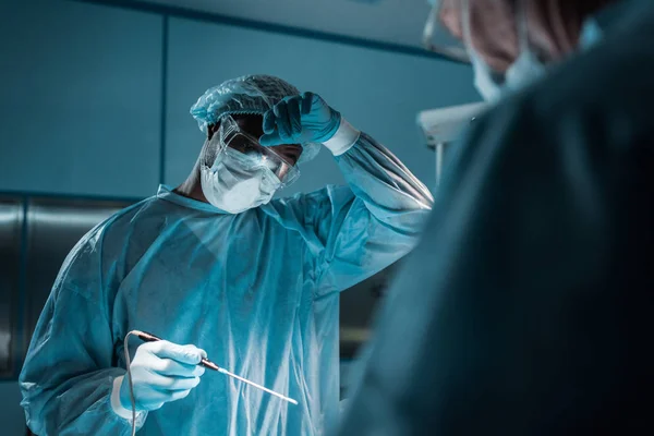 Cirurgião afro-americano tocando na testa durante a cirurgia — Fotografia de Stock