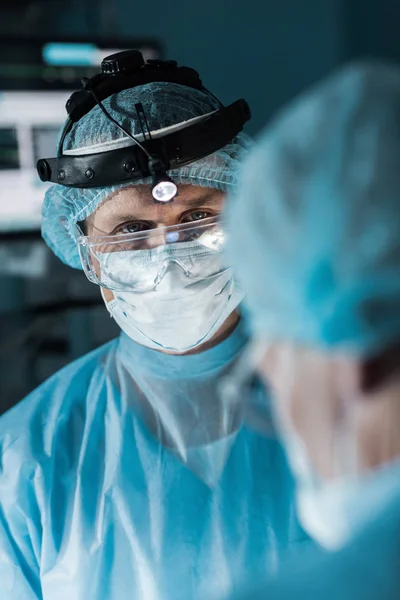 Surgeon in medical mask looking at colleague in surgery room — Stock Photo