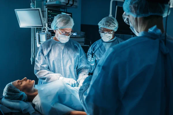Мультикультурные хирурги, оперирующие пациентку — стоковое фото