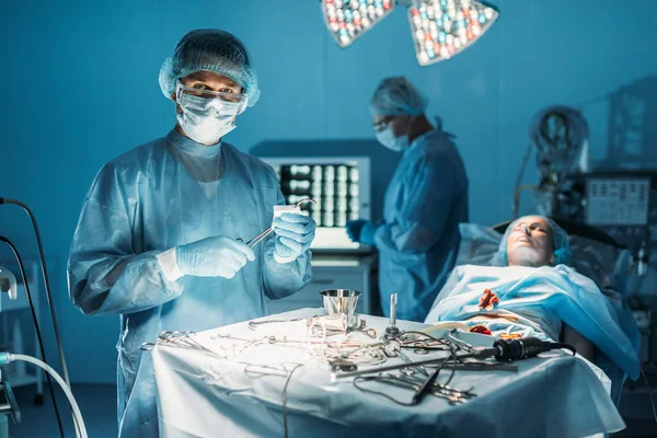 Cirujano limpiando pinzas quirúrgicas y mirando la cámara en la sala de cirugía - foto de stock