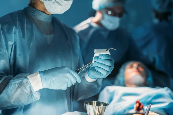 Imagen recortada de cirujano limpiando pinzas quirúrgicas en sala de cirugía - foto de stock