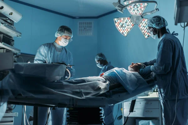 Médicos multiculturais preparando paciente para cirurgia na sala de cirurgia — Fotografia de Stock