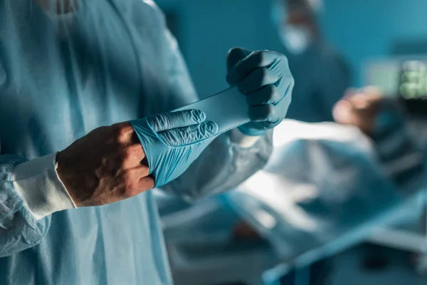 Image recadrée du chirurgien enlevant des gants médicaux dans la salle d'opération — Photo de stock