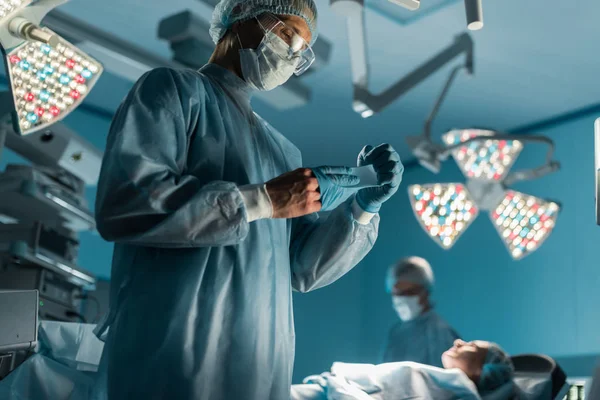 Cirurgião tirando luvas médicas perto do paciente na sala de cirurgia — Fotografia de Stock