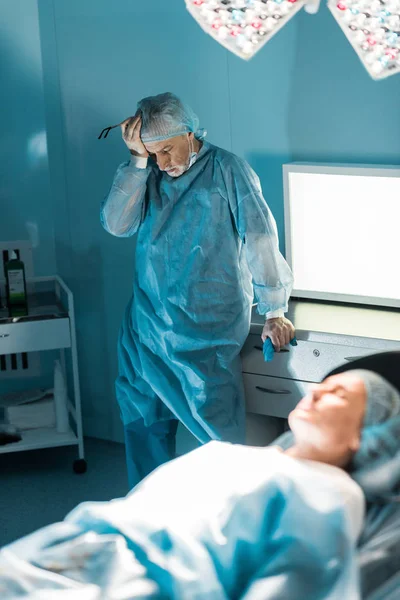 Exhausted doctor standing near patient in surgery room — Stock Photo