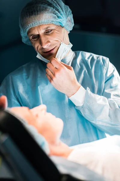 Médico sonriente mirando al paciente en la sala de cirugía - foto de stock