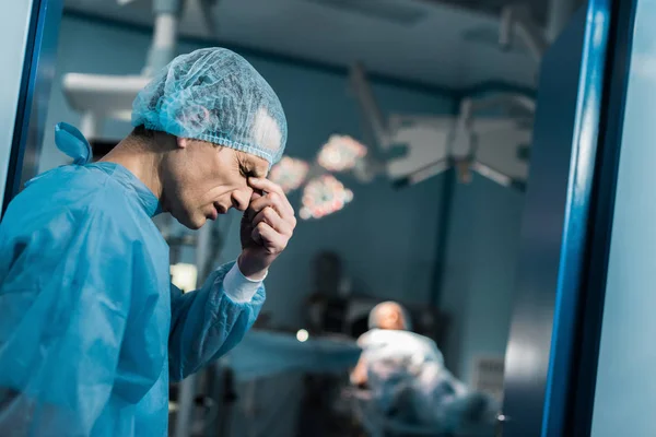 Vista lateral do médico cansado tocando ponte do nariz na sala de cirurgia — Fotografia de Stock