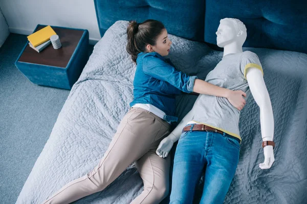 Alta vista angular de la mujer abrazando maniquí en la cama, concepto de amor unidireccional - foto de stock