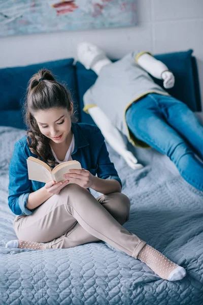Woman reading book while resting on bed with mannequin, loneliness concept — Stock Photo