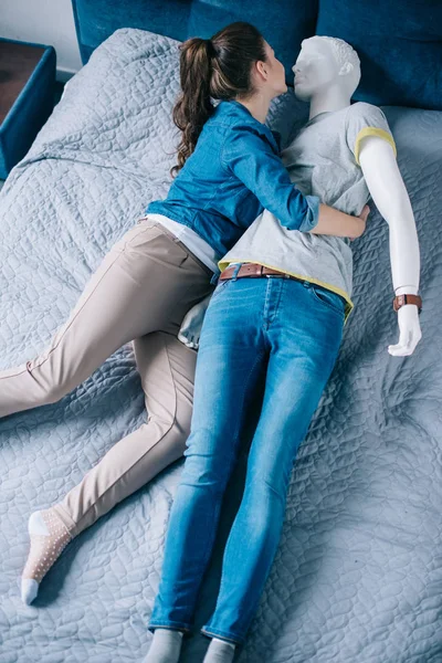 Alta vista angular de la mujer abrazando maniquí en la cama, concepto de amor unidireccional - foto de stock