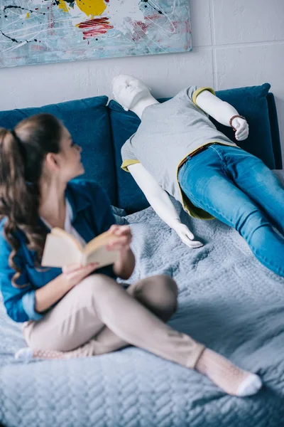 Selective focus of woman with book resting on bed with mannequin, loneliness concept — Stock Photo