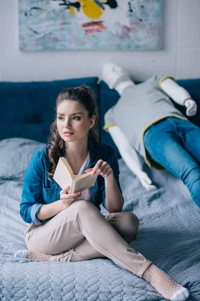 Donna triste con libro appoggiato sul letto con manichino, concetto di solitudine — Foto stock