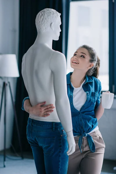 Vue latérale de femme heureuse avec tasse de café étreignant mannequin, concept d'amour à sens unique — Photo de stock