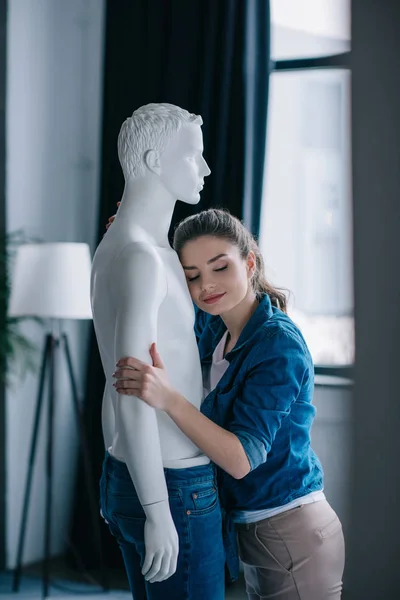 Vue latérale de sourire jeune femme étreignant poupée profane, concept d'amour à sens unique — Photo de stock