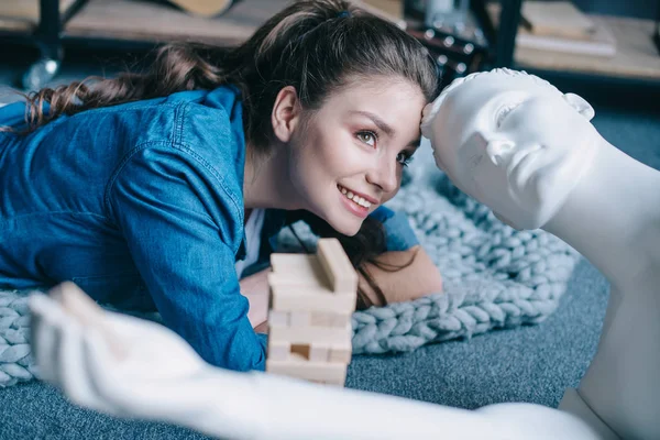 Beautiful woman lying near mannequin and blocks wood game on floor at home, loneliness concept — Stock Photo