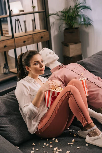 Mujer comer palomitas de maíz mientras ve la película junto con maniquí en casa, concepto de sueño relación perfecta - foto de stock