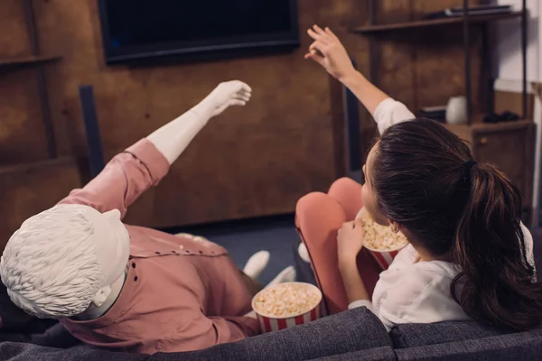 Rückansicht einer Frau, die Popcorn isst, während sie zu Hause zusammen mit einer Schaufensterpuppe Film guckt, perfektes Beziehungstraum-Konzept — Stockfoto