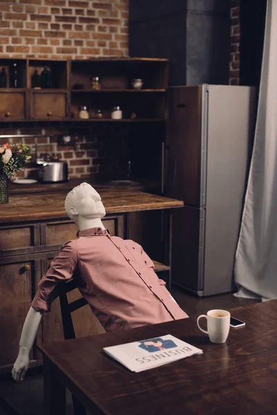 Close up view of manikin at table with cup of coffee and newspaper in kitchen — Stock Photo