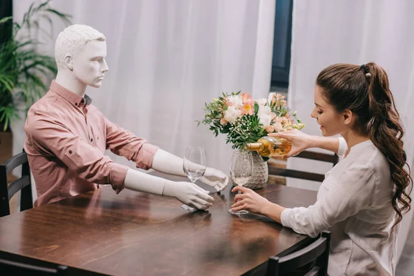 Femme verser du vin dans le verre tout en étant assis à table avec poupée profane, concept d'amour non partagé — Photo de stock