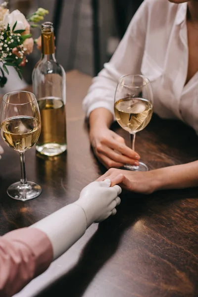 Cropped shot of woman and mannequin holding hands at table with glasses of wine, unrequited love concept — Stock Photo