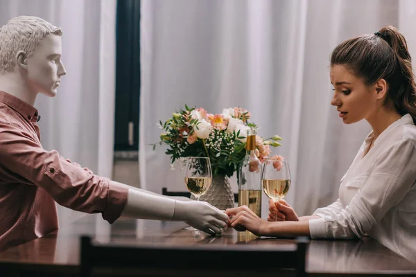 Vista lateral de la mujer con copa de vino sentado en la mesa con la muñeca laico, concepto de amor no correspondido - foto de stock