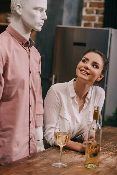 Mujer sonriente mirando maniquí en la mesa con gafas de vino en casa, concepto de sueño relación perfecta - foto de stock
