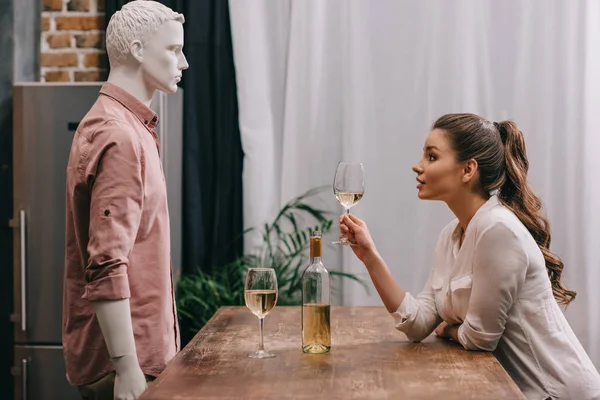 Side view of young woman with glass of wine at table with male manikin, unrequited love concept — Stock Photo